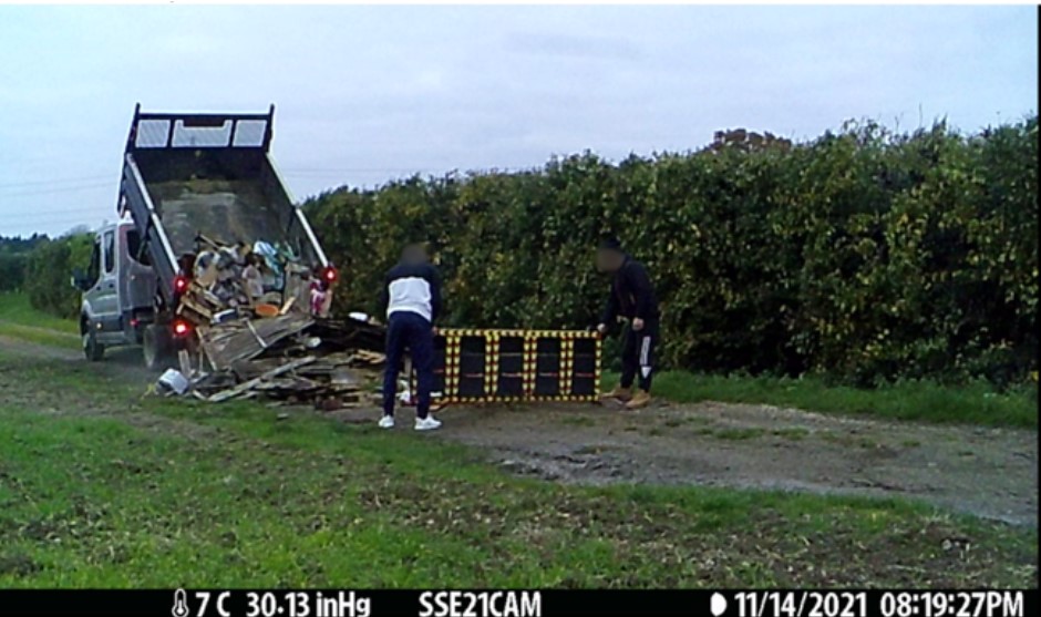 The image shows the back of a van dropping some building materials onto some grass.