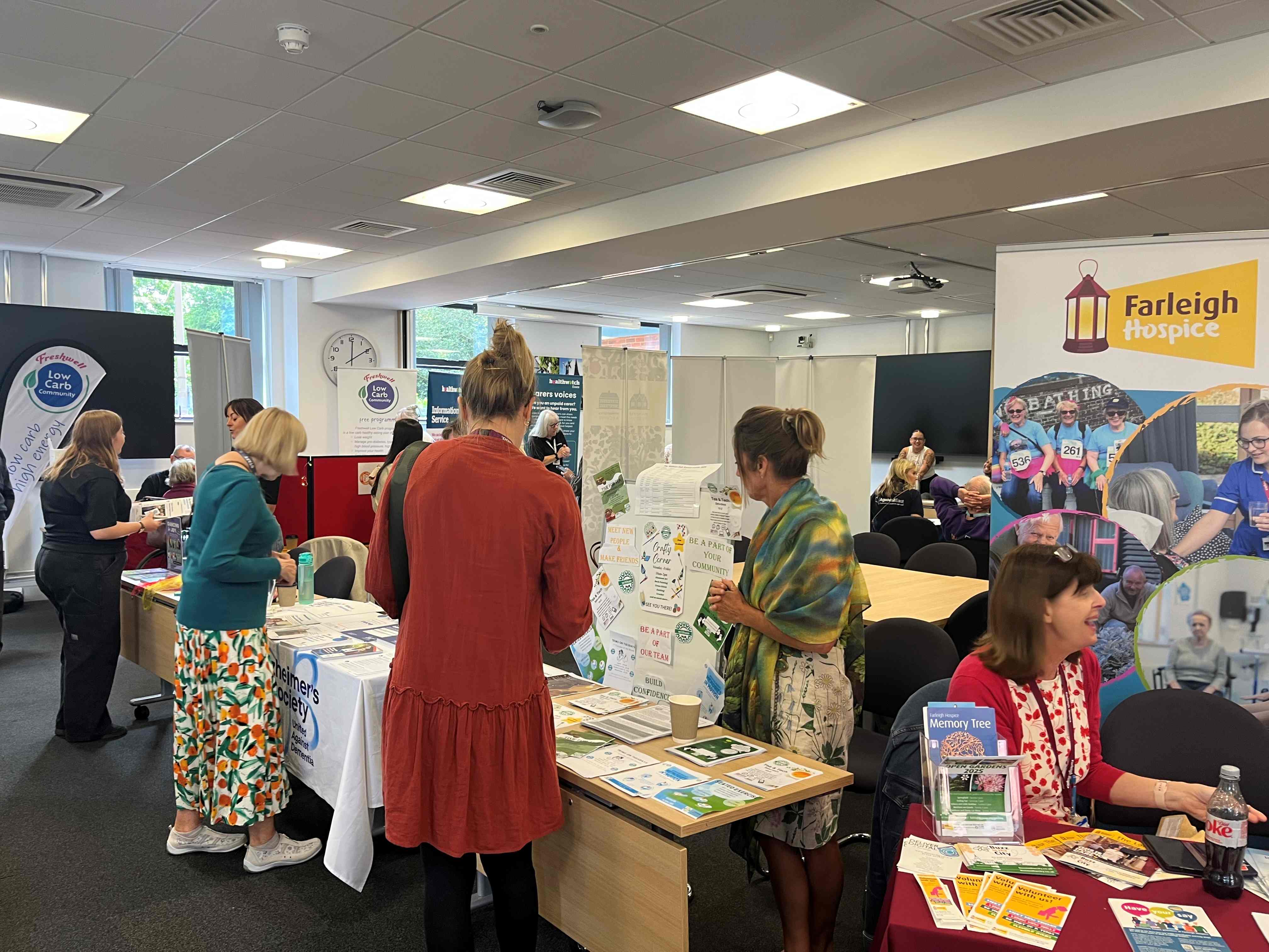 The image shows a group of people at an event, visiting stalls.