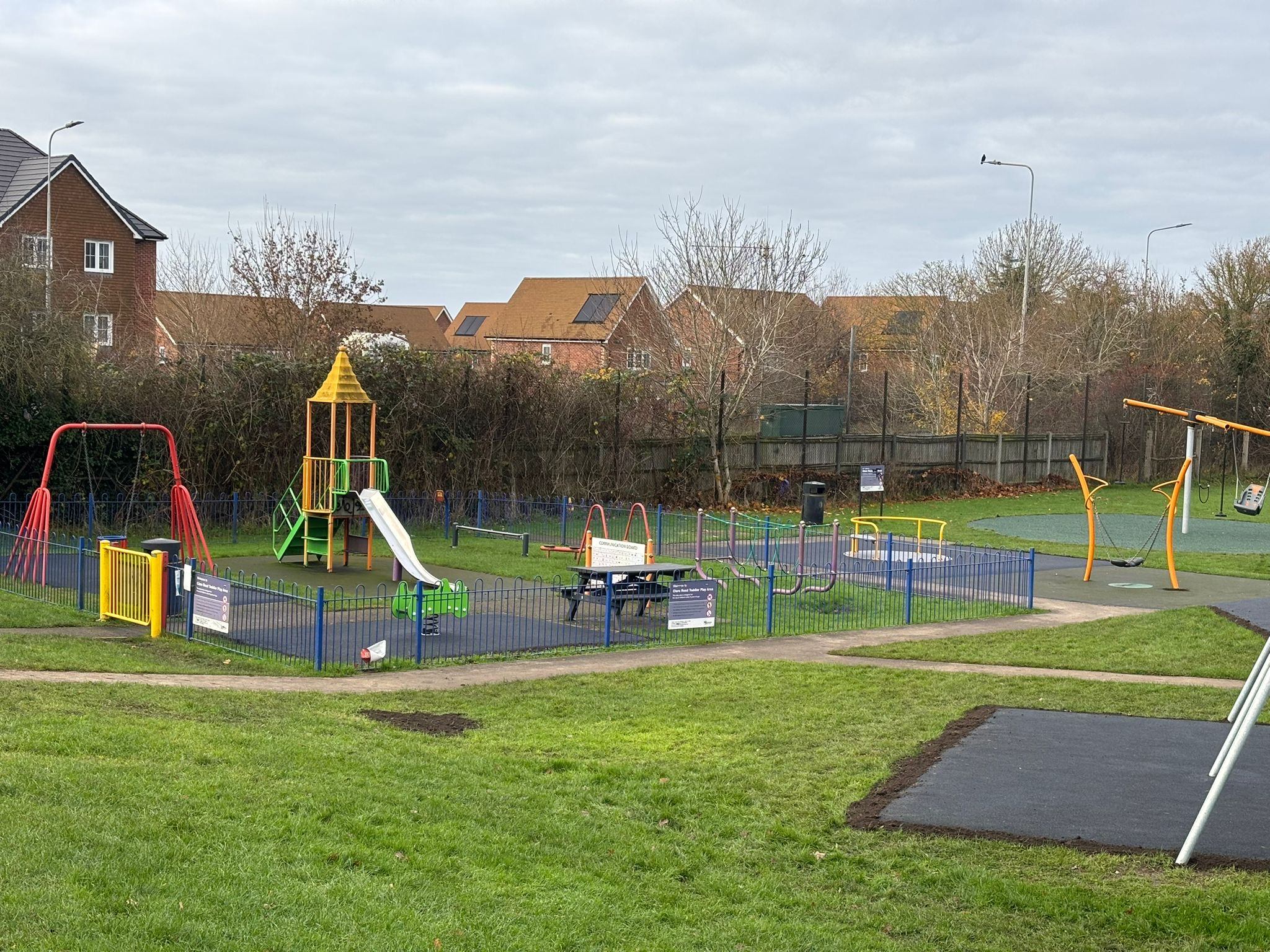 The image shows a playground in the foreground on a large green space with houses in the background.