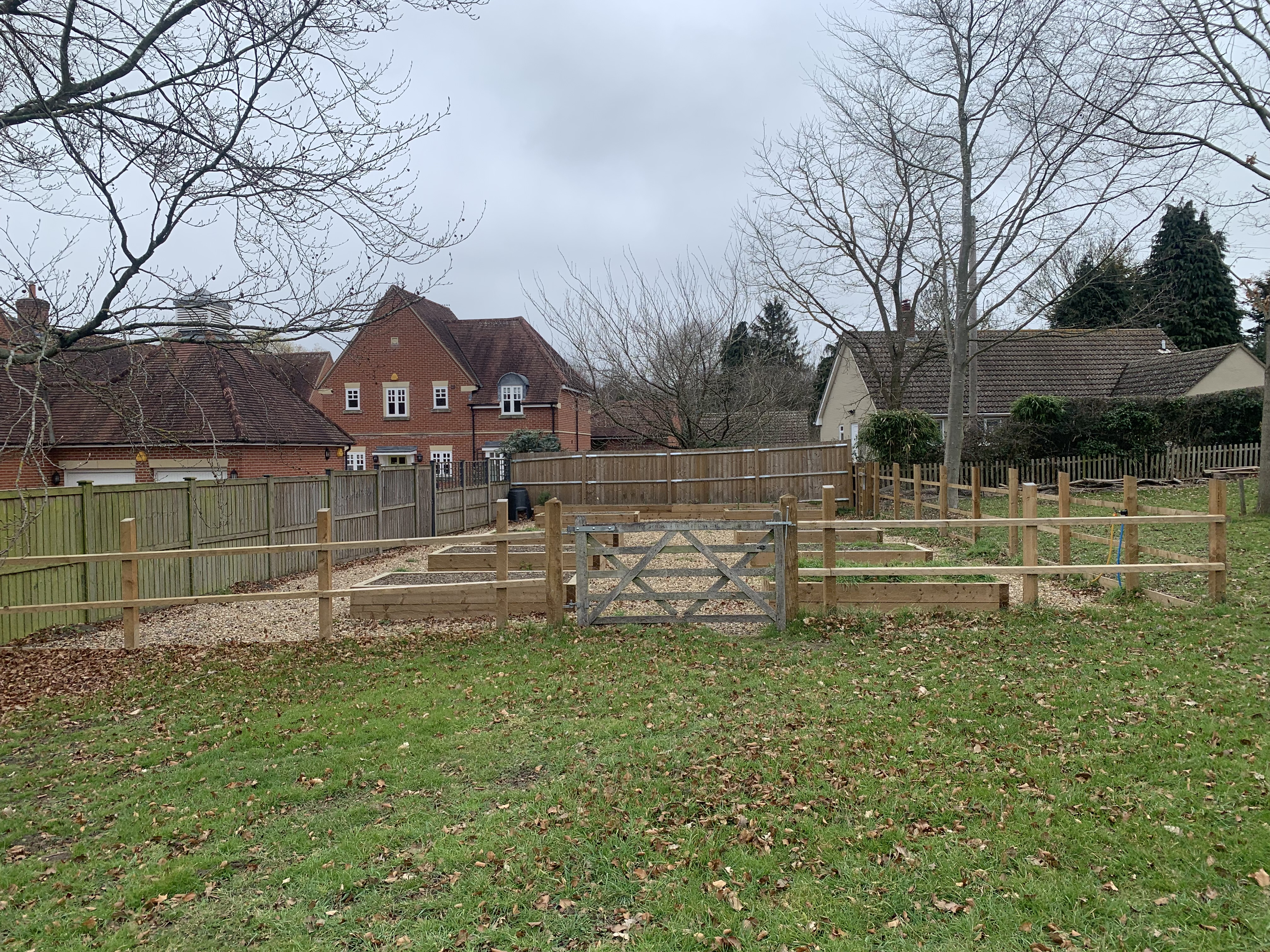 A gate with a fence around a small bit of land with gardens beds planted.