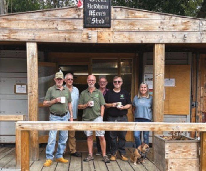 Photo of Great Yeldhams Men's Shed, with members on the deck holding drinks