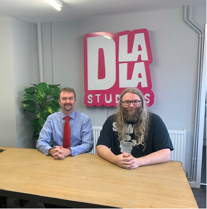 Two people are sitting at a table facing the camera with the Dlala logo behind them.