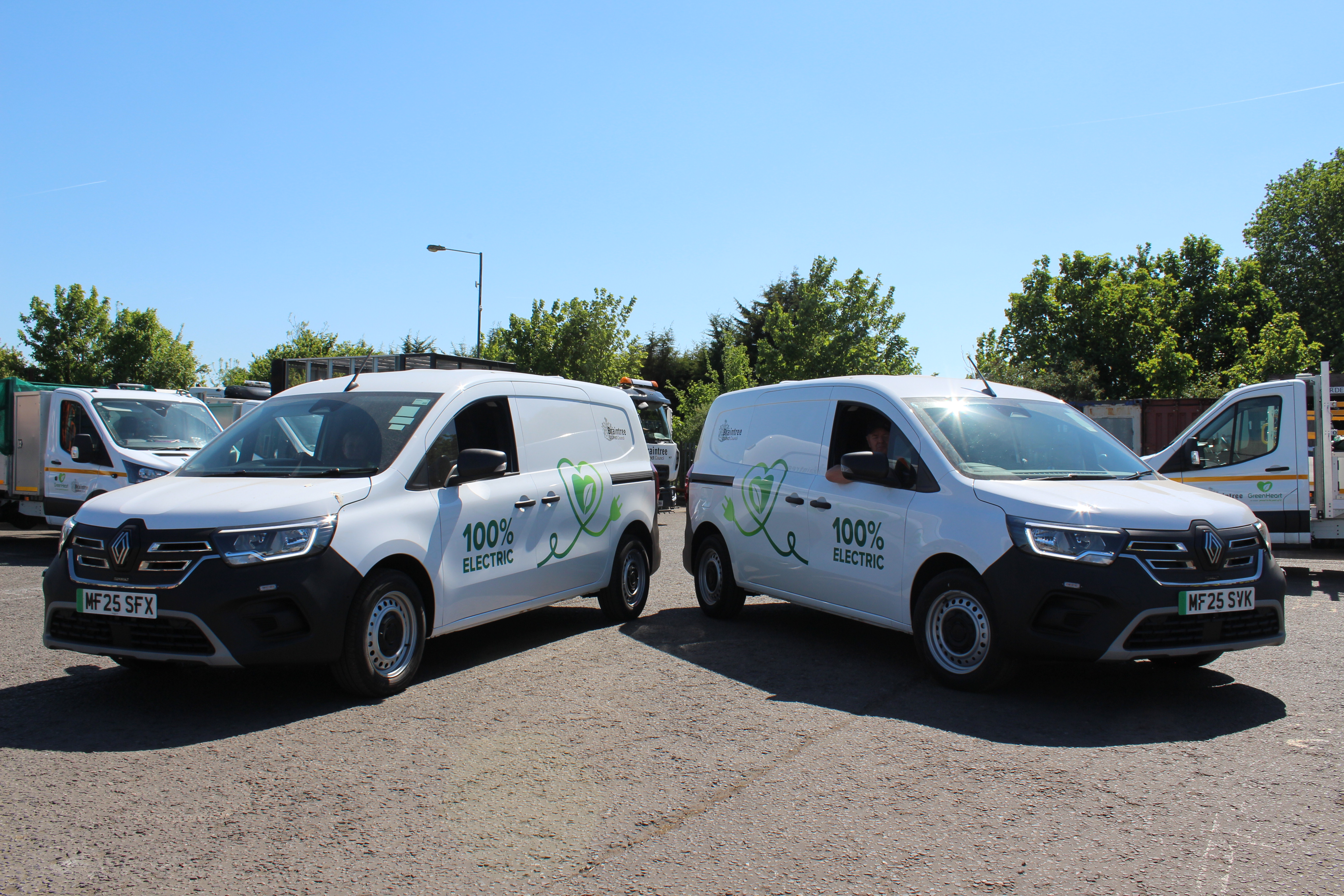Two electric vans, parked back to back and facing outwards away from each other so you can see the words 100% electric on their rears.