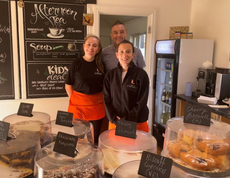 Photo of Fox in the Stables tea room, displaying staff behind a counter of cakes in cakestands