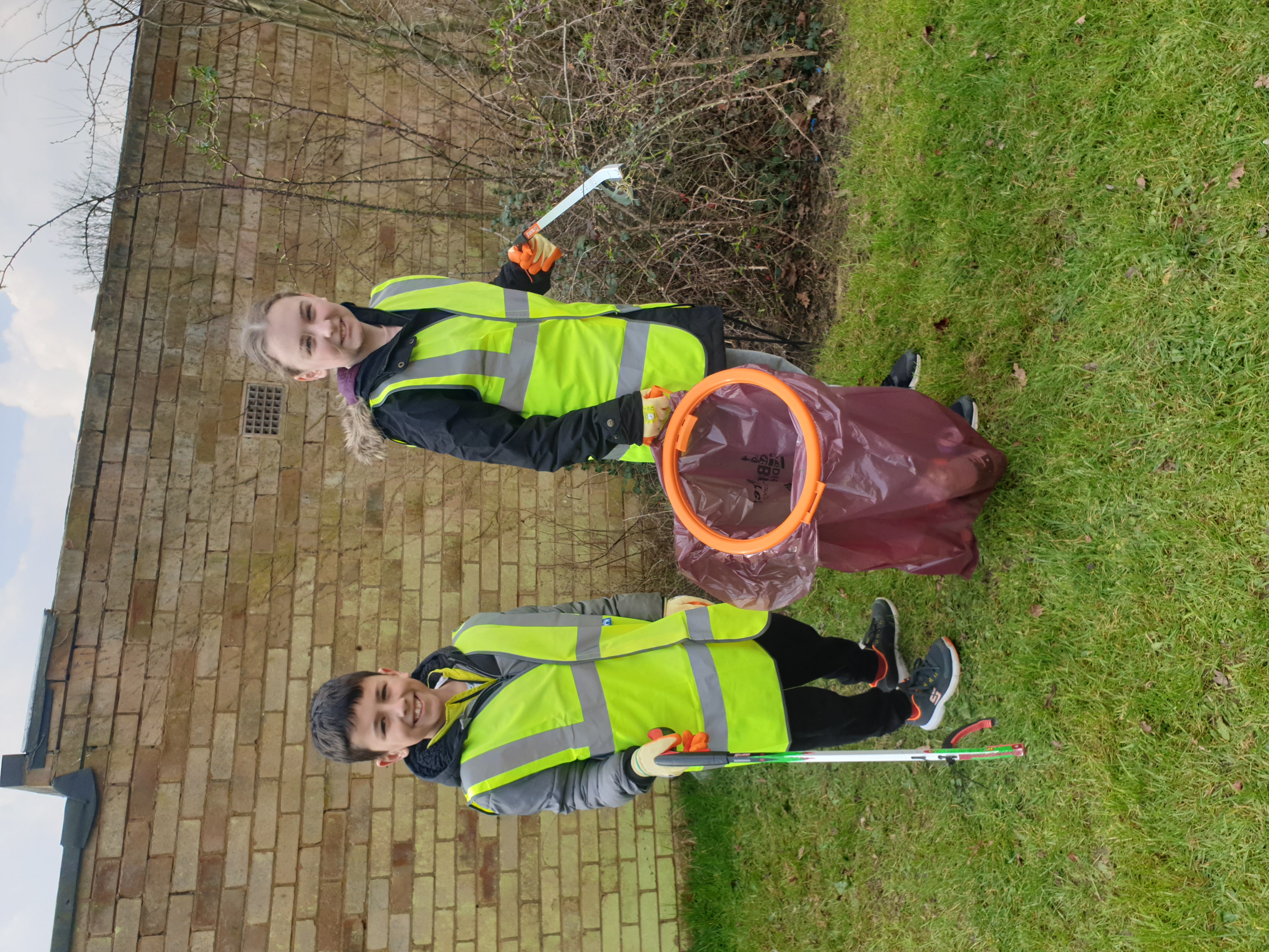 Two children in high vis jackets picking up litter
