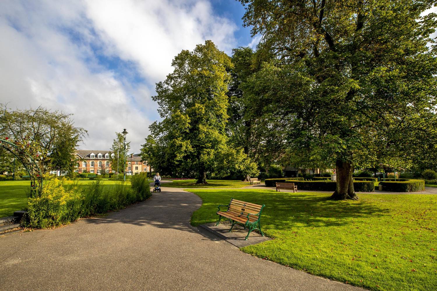 Image - Halstead Public Gardens with a women walking on a path near trees and field.