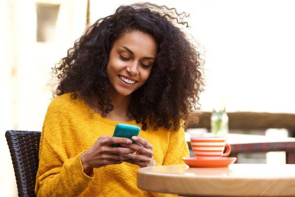 A women in a yellow jumper holding a phone and smiling