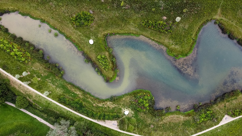 A birds eye view of a park field and a flood prevention pond next to a footpath