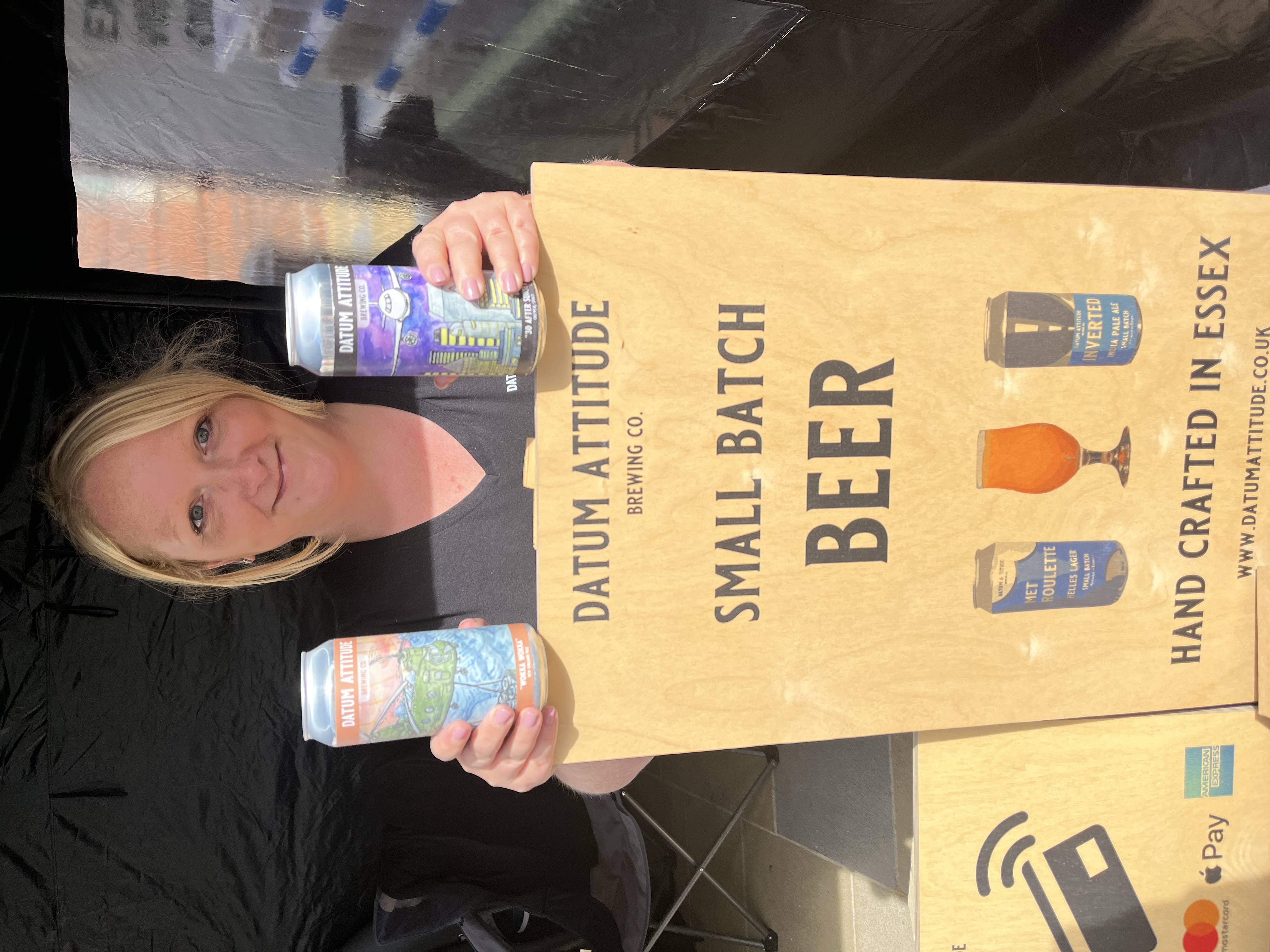 Owner of Datum Atttitude beer stands behind sign with two cans in her hands