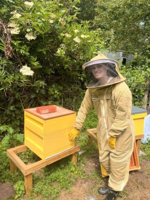 Photo of Amy Bearman in beekeeper protective clothing in front of a beehive