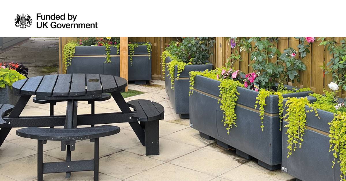 The image shows a small garden with planters and a picnic table with seating
