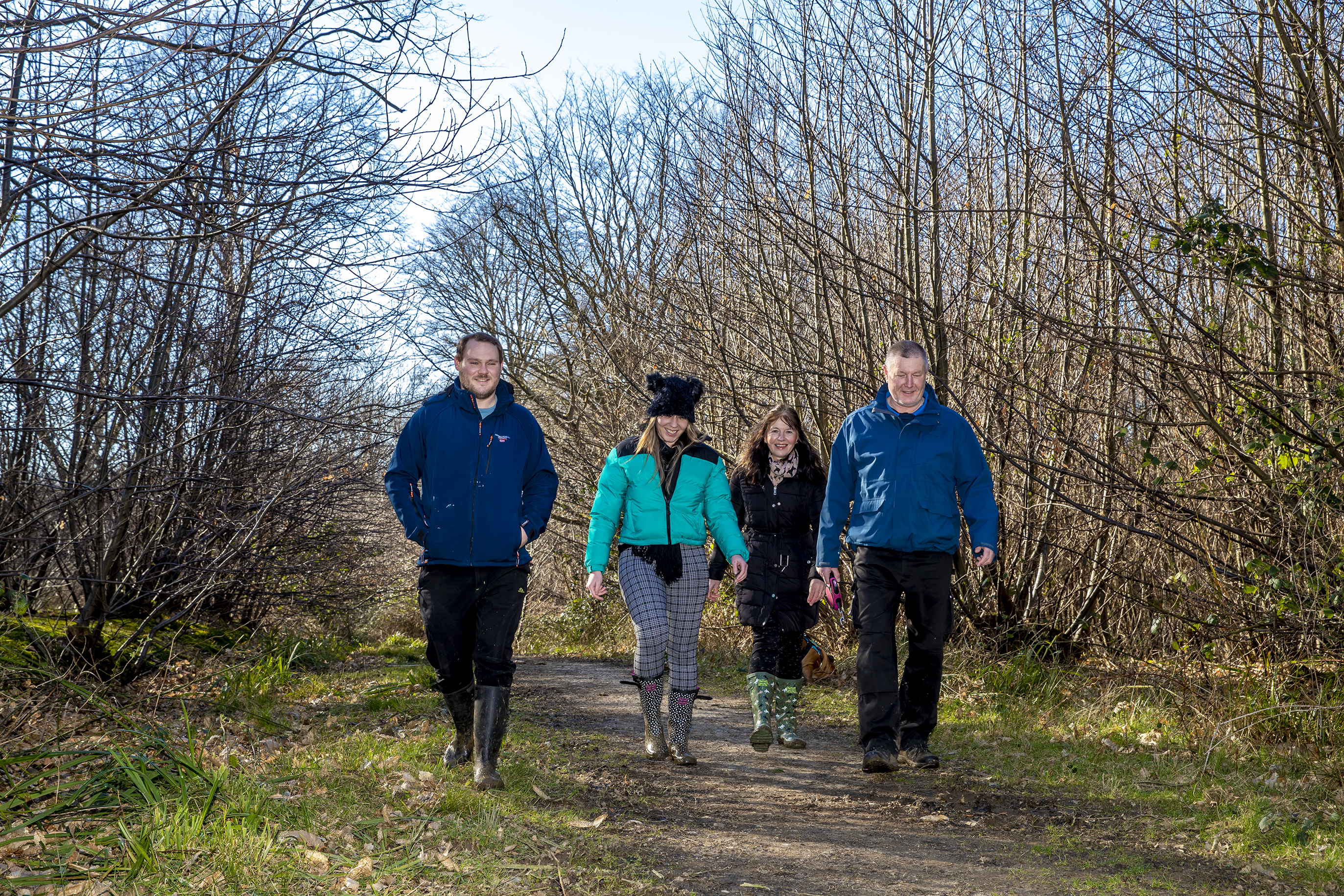 The image shows 4 adults walking in the woods.