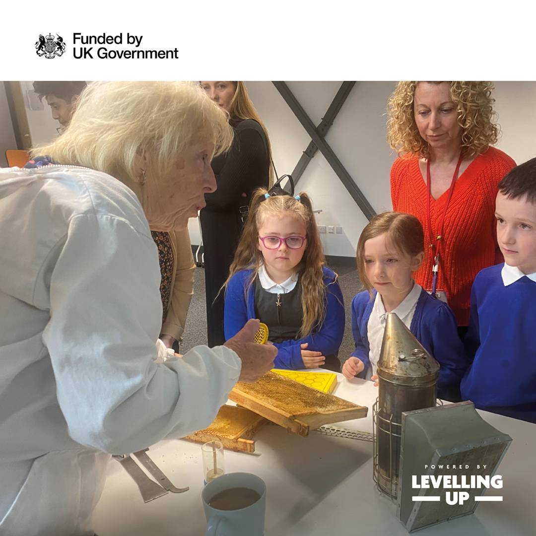 A woman animatedly shows three children and their teacher a piece of honeycomb.