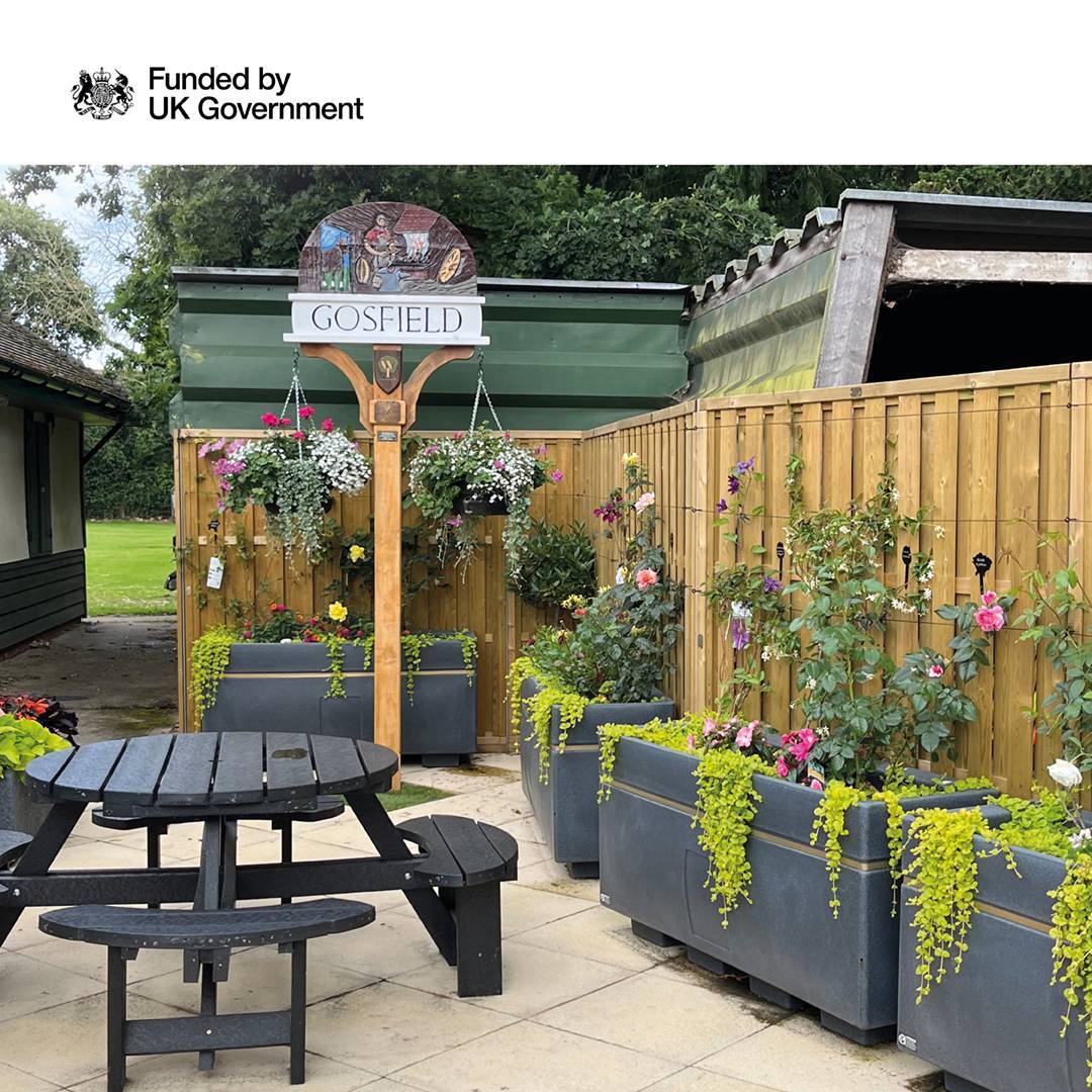 A gate with a fence around a small bit of land with gardens beds planted.