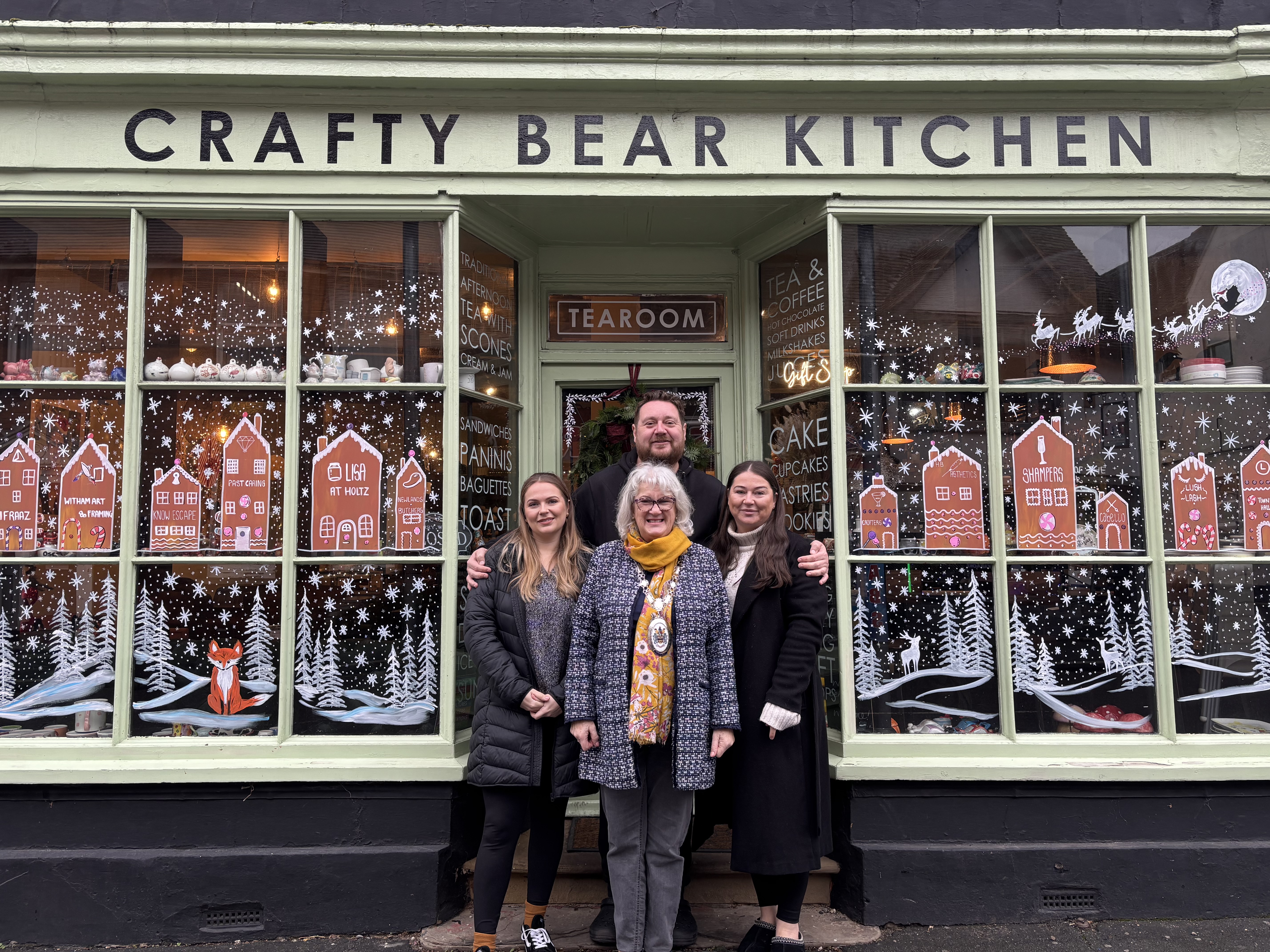 Chairman and owners of Crafty Bear Kitchen stand outside next to window display.